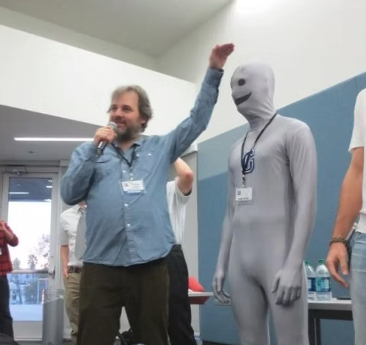 Dan Harmon holding a microphone beside a fan dressed as the Greendale Human Being